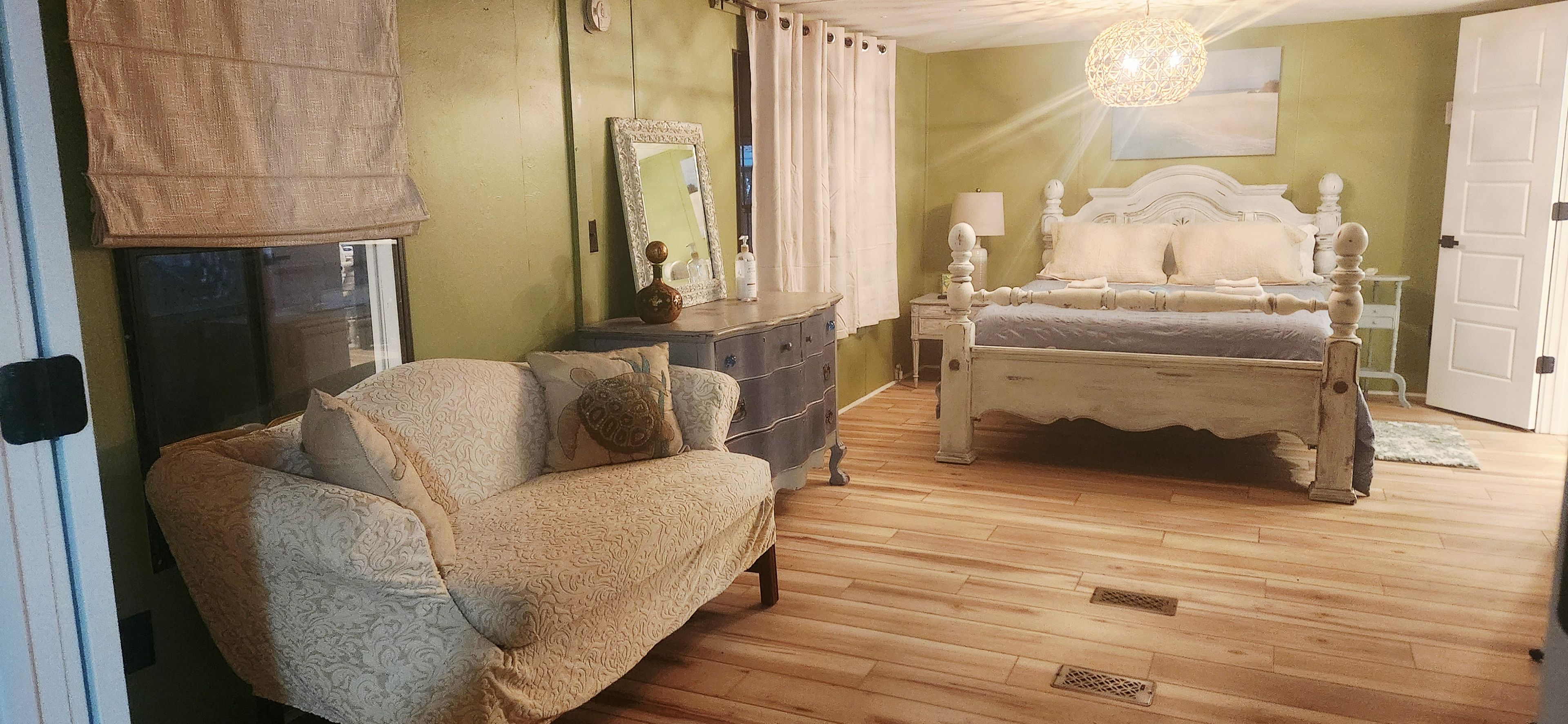 A bedroom with a bed, a dresser, a chair, a mirror, and a hanging light fixture.