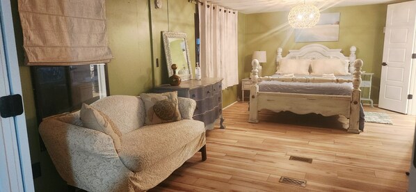 A bedroom with a bed, a dresser, a chair, a mirror, and a hanging light fixture.