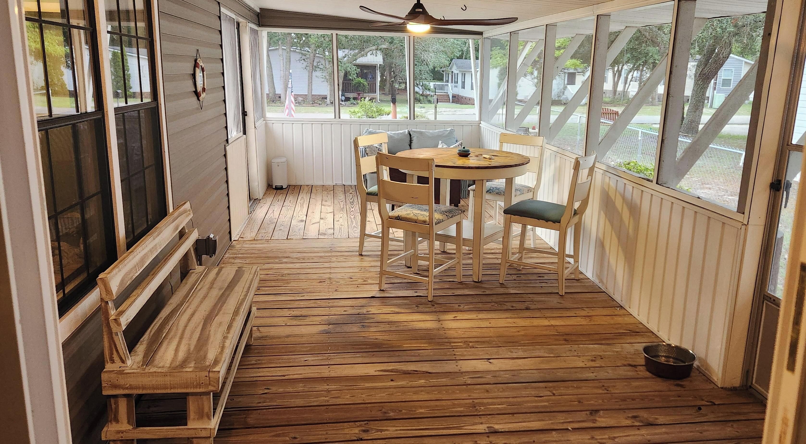 A covered porch with a wooden table and chairs, a bench, and a view of the outside.