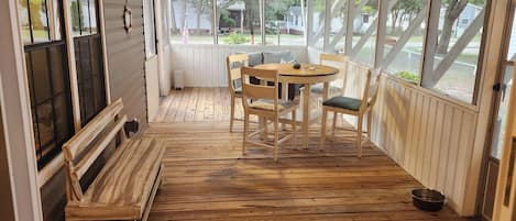 A covered porch with a wooden table and chairs, a bench, and a view of the outside.