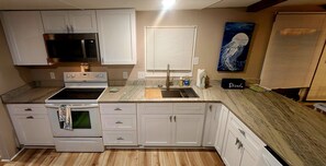 A kitchen with white cabinets, a microwave, an oven, a sink, and a window with blinds. - Sunset Tides & Tales! Boat Parking - Prime Location - Screen Porch & Sunroom (Sunset Beach)