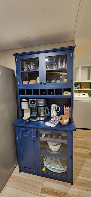 A blue kitchen cabinet with shelves containing glassware, a coffee maker, and a microwave.