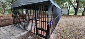 A black metal dog kennel with a roof, a metal door, and a blue toy attached to the door.