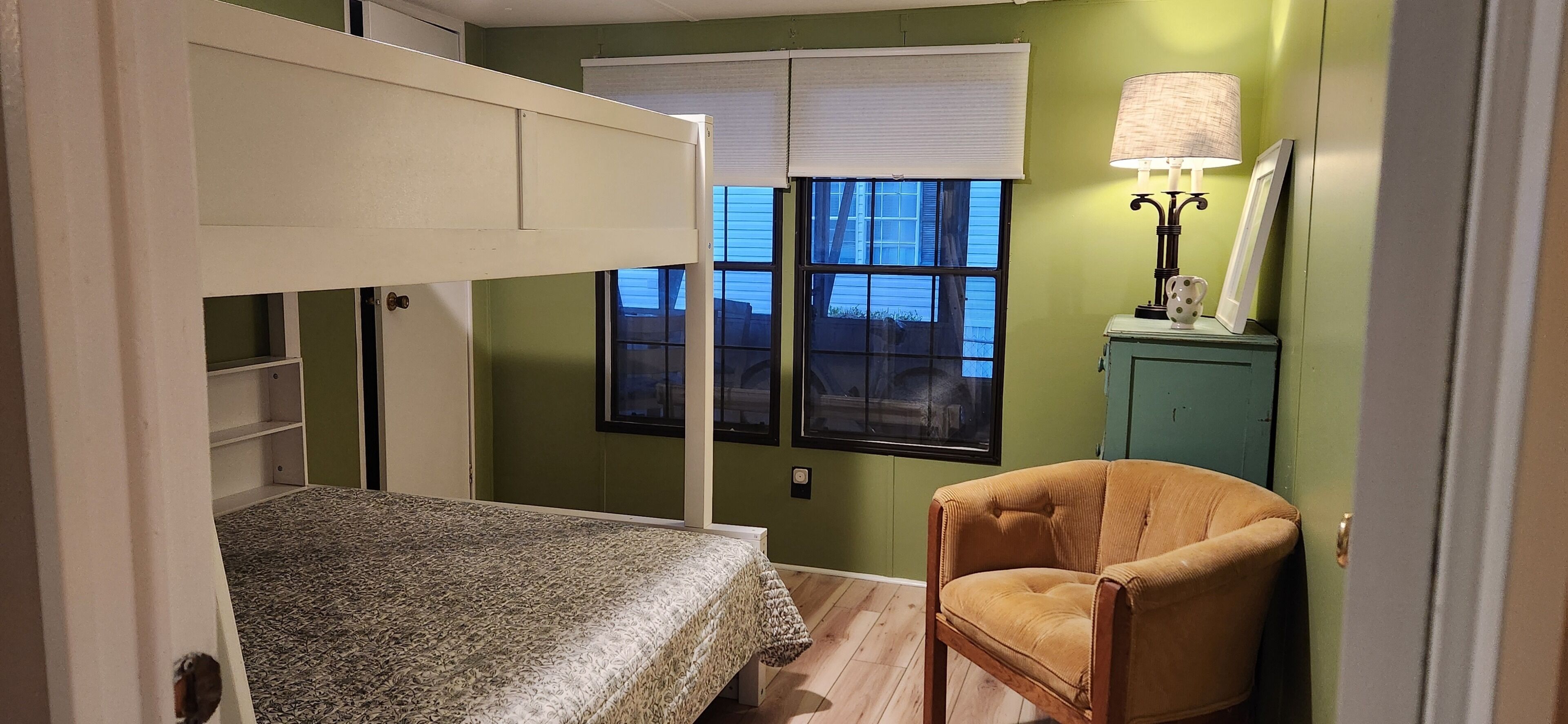 A room with bunk beds, a chair, a window with blinds, and a lamp.