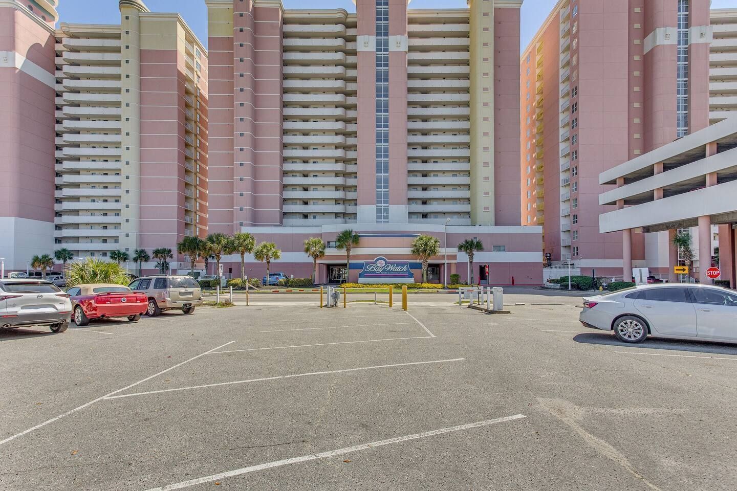 Un parcheggio con diverse auto, un edificio di un hotel con un cartello 'Bay Watch' e un segnale 'STOP'.