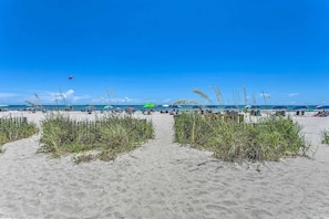 Een strand met zand, strandparasols en mensen.
