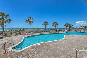A swimming pool with lounge chairs and palm trees, overlooking a beach. - Seas the Day with Ocean Views & a Lazy River (North Myrtle Beach)