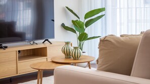 A modern living room with a flat-screen TV on a wooden stand, a round wooden coffee table, two striped vases, a large green plant, and a beige sofa. - Polacos Residence | 2BR | Apt J by LovelyStay (Vila Nova de Gaia)