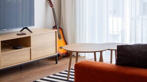 A modern living room with a television, a guitar, a wooden cabinet, a round table, and a striped rug. - Polacos Residence | 2BR | Apt Q by LovelyStay (Vila Nova de Gaia)