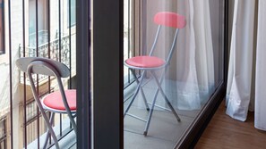 Zwei zusammenklappbare Stühle mit roten Kissen, platziert in der Nähe eines Fensters mit Blick auf ein Gebäude.