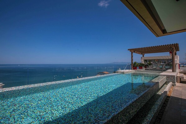 Une piscine avec vue sur l’océan, une pergola et un espace de détente.