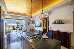 Une cuisine moderne dotée d’un îlot central, de luminaires suspendus et offrant une vue sur l’espace extérieur aménagé pour se détendre.