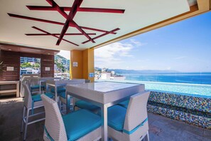 A sunlit outdoor seating area with a view of the ocean, featuring a poolside bar and lounge chairs. - Amazing V177 Ocean Chic (Puerto Vallarta)