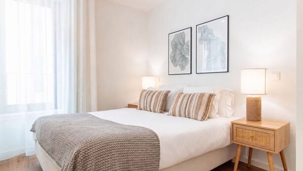 A neatly made bed with a striped blanket, two wall-mounted lamps, and two framed floral artworks. - Polacos Residence | 2BR | Apt H by LovelyStay (Vila Nova de Gaia)