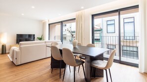 A modern living room with a sofa, dining table, and chairs, a flat-screen TV, and large windows with a view of the city. - Polacos Residence | 2BR | Apt H by LovelyStay (Vila Nova de Gaia)