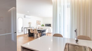Eine moderne Küche mit Essbereich, weißen Schränken und einem großen Fenster mit Vorhängen.