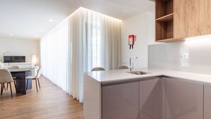 Eine moderne Küche mit integrierter Kochinsel, einem Essbereich inklusive Sofa und Stühlen sowie einem großen Fenster mit transparenten Vorhängen.