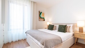 Ein Hotelzimmer mit Bett, Nachttisch, Lampe, einem Bild an der Wand und transparenten Vorhängen.
