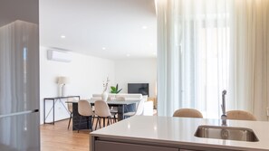 Una cocina moderna con una isla grande, un comedor con sillas, un televisor y una planta.