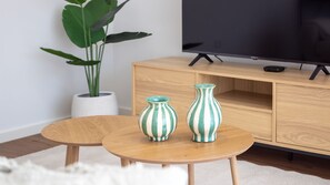A room with a wooden TV stand, a flat-screen TV, two striped vases, a round wooden table, and a potted plant. - Polacos Residence | 2BR | Apt S by LovelyStay (Vila Nova de Gaia)