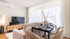 Ein modernes Wohnzimmer mit Flachbildfernseher, einem Esstisch für zwei Personen und einer Couch.
