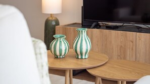 Ein Zimmer mit einem runden Holztisch, zwei gestreiften Vasen, einem Fernseher und einer Lampe.