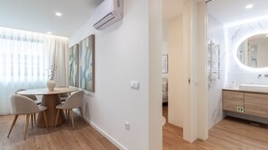 Ein modernes Hotelzimmer mit Essbereich, einem Badezimmer mit Marmorwaschtisch und einem großen Fenster mit transparenten Vorhängen.