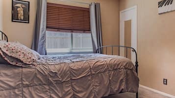 A bedroom with a bed, a window with blinds, a door, and a wall-mounted light switch.