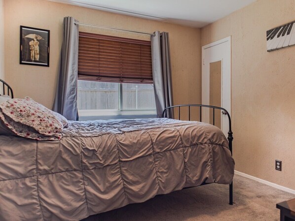 A bedroom with a bed, a window with blinds, a door, and a wall-mounted light switch.
