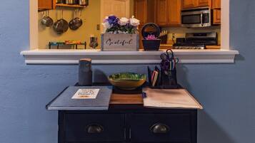 A kitchen with wooden cabinets, a microwave, and a shelf with cooking utensils.