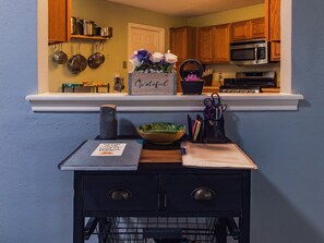 Una cocina con armarios de madera, microondas y un estante con utensilios de cocina.