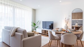 Ein modernes Wohnzimmer mit Sofa, Fernseher, Esstisch und Stühlen.
