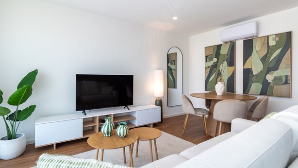 Una sala de estar moderna con un televisor de pantalla plana, un sofá blanco, una mesa de centro y una zona de comedor con sillas.