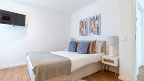 Un dormitorio con cama, mesitas de noche, lámpara y cuadros en la pared.