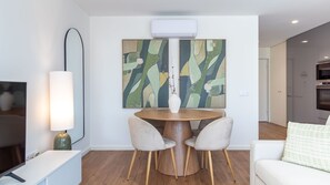 A modern living room with a round wooden table, two chairs, a flat-screen TV, and a large abstract painting above the table. - Polacos Residence | 1BR | Apt Y by LovelyStay (Vila Nova de Gaia)