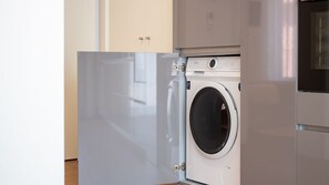 A compact, modern laundry room with a front-loading washing machine, a dryer, and a cabinet with a lock. - Polacos Residence | 1BR | Apt Y by LovelyStay (Vila Nova de Gaia)