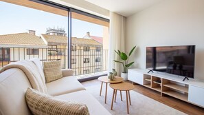 A modern living room with a sofa, TV, and a view of buildings through large windows. - Polacos Residence | 1BR | Apt Y by LovelyStay (Vila Nova de Gaia)