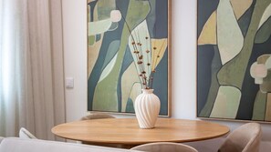 A dining area with a round wooden table, a white vase with dried flowers, and abstract paintings on the wall. - Polacos Residence | 1BR | Apt AA by LovelyStay (Vila Nova de Gaia)