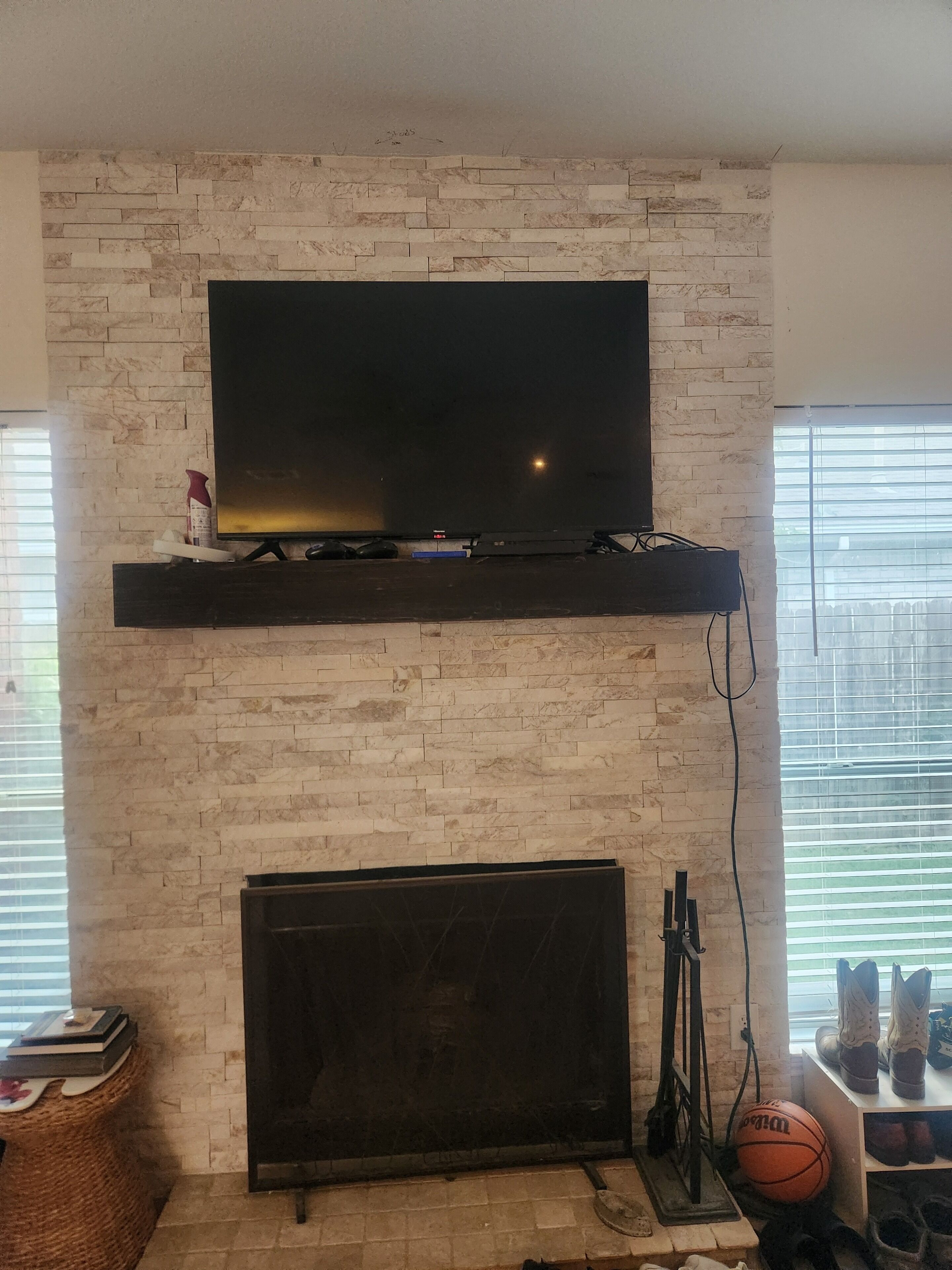 A living room with a brick wall, a mounted flat-screen TV, a fireplace, and a window with blinds.