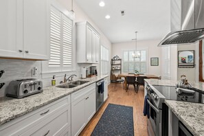 A modern kitchen with white cabinets, a granite countertop, stainless steel appliances, and a dining area with a wooden table and chairs. - Downtown Delight on Main Street - Brevard, NC (Brevard)