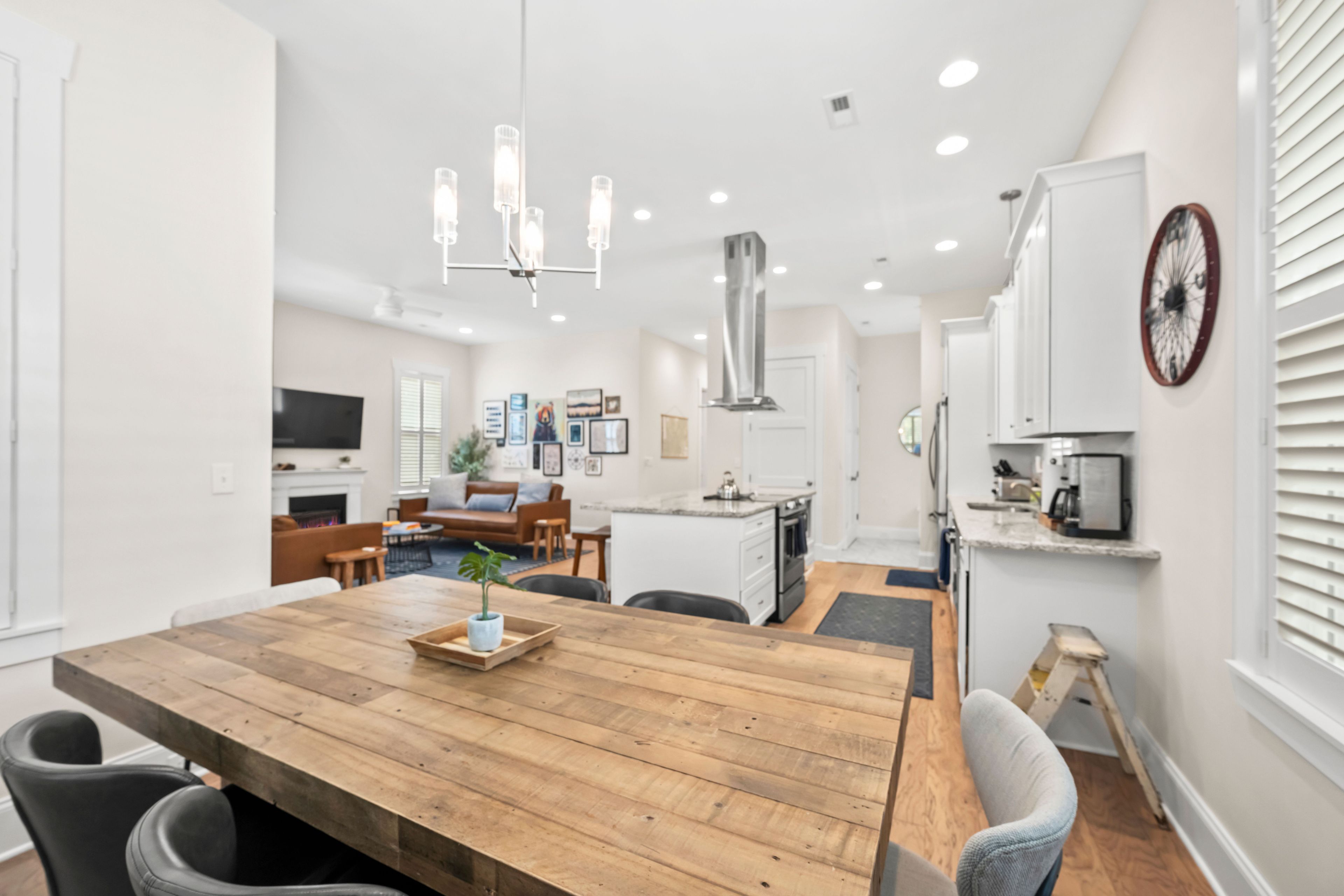 A modern kitchen with white cabinets, a wooden dining table, and a central island.