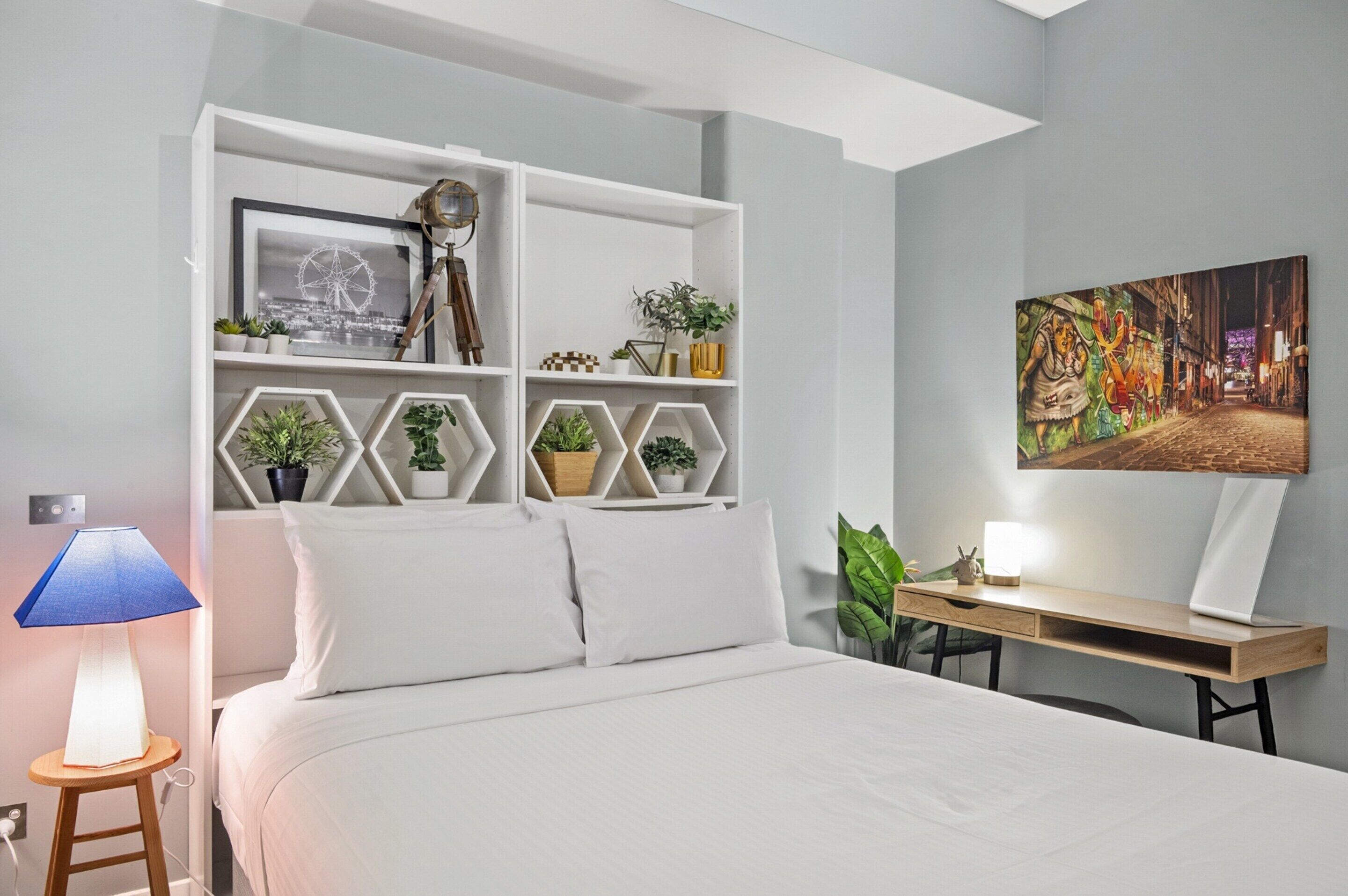 A bedroom with a bed, a desk, and a wall-mounted shelf with decorative items.