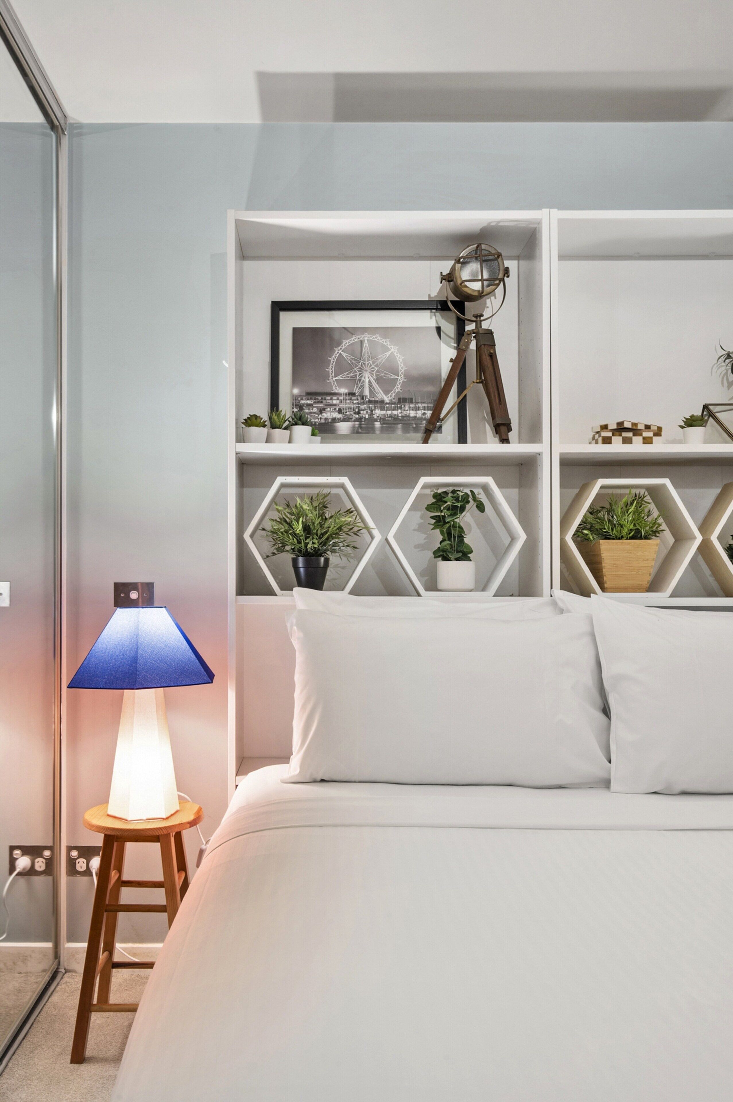 Ein ordentlich eingerichtetes Schlafzimmer mit Bett, Nachttischlampe, einem Regal mit Dekoration und einem an der Wand befestigten Teleskop.