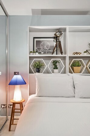 A neatly arranged bedroom with a bed, a bedside lamp, a shelf with decorative items, and a wall-mounted telescope. - Temple Court Suite in Melbourne CBD (Melbourne)
