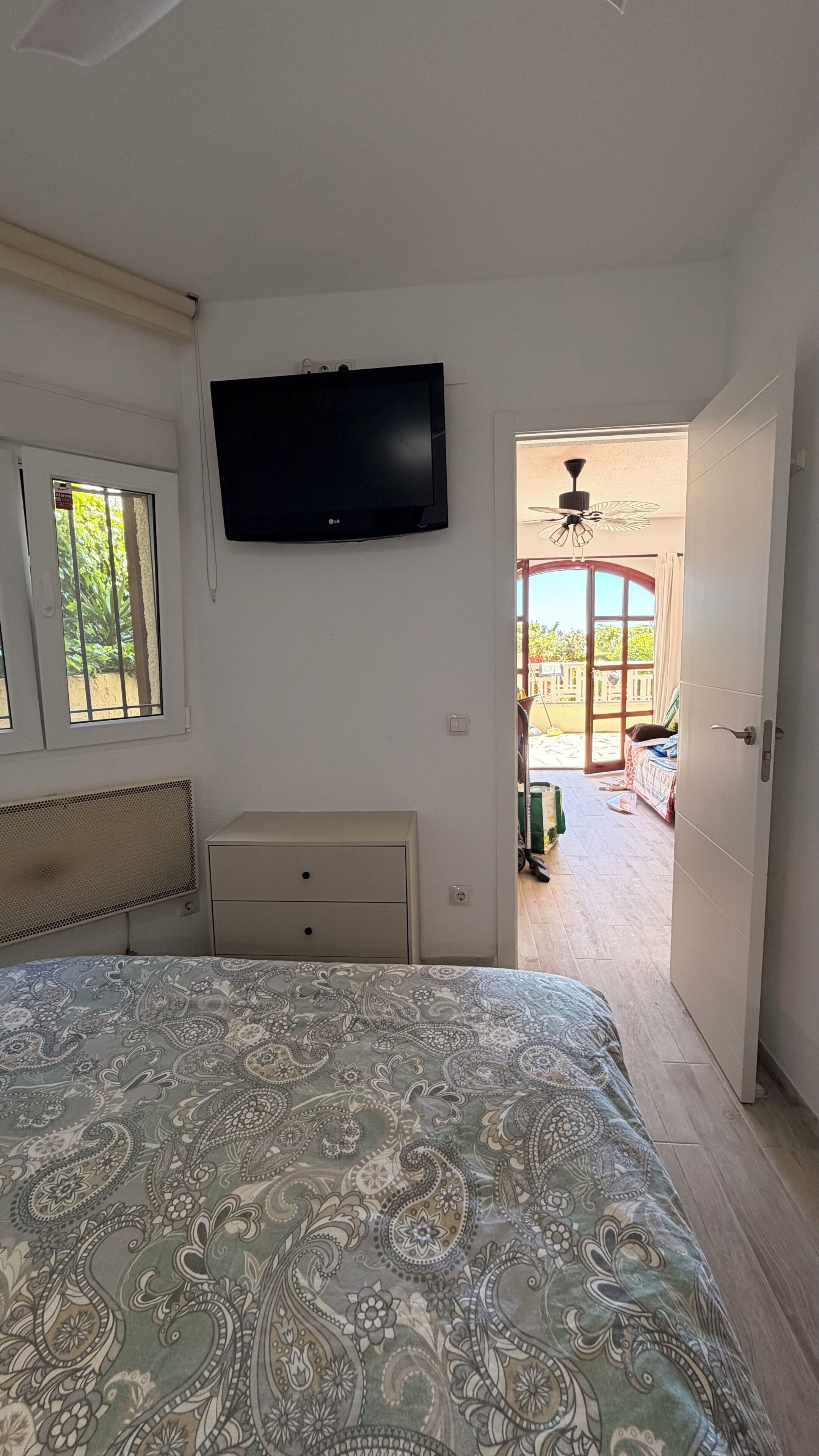 Una camera da letto con un letto, una televisione, una finestra e una porta aperta che dà su un balcone.
