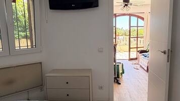 Una camera da letto con un letto, una televisione, una finestra e una porta aperta che dà su un balcone.