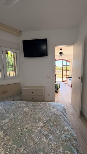 Una camera da letto con un letto, una televisione, una finestra e una porta aperta che dà su un balcone.