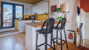 Une cuisine moderne dotée d’un îlot central, de tabourets de bar, d’une machine à café et offrant une vue sur l’extérieur grâce à une grande fenêtre.