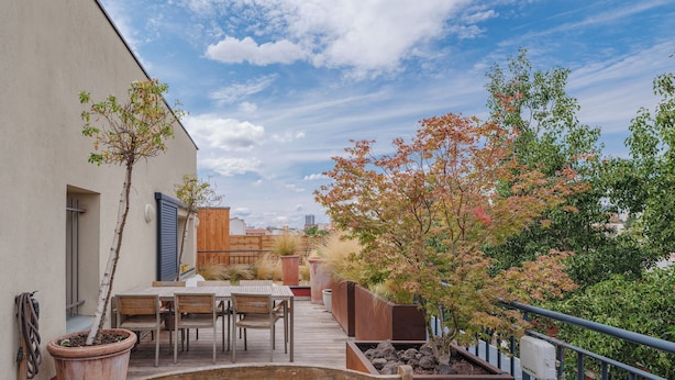 Une terrasse sur le toit, avec une table et des chaises en bois, des plantes en pot et une vue sur le paysage urbain.
