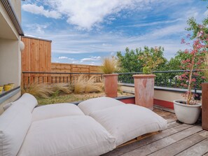 Ein Balkon mit Holzboden, einer weißen Sitzgelegenheit mit Kissen und Topfpflanzen.